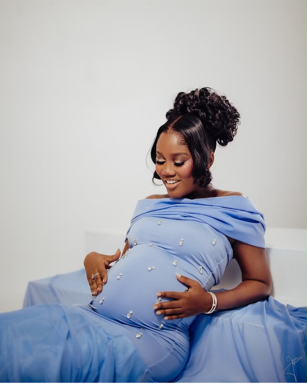 Expectant mother in a blue gown smiling while cradling her bump
