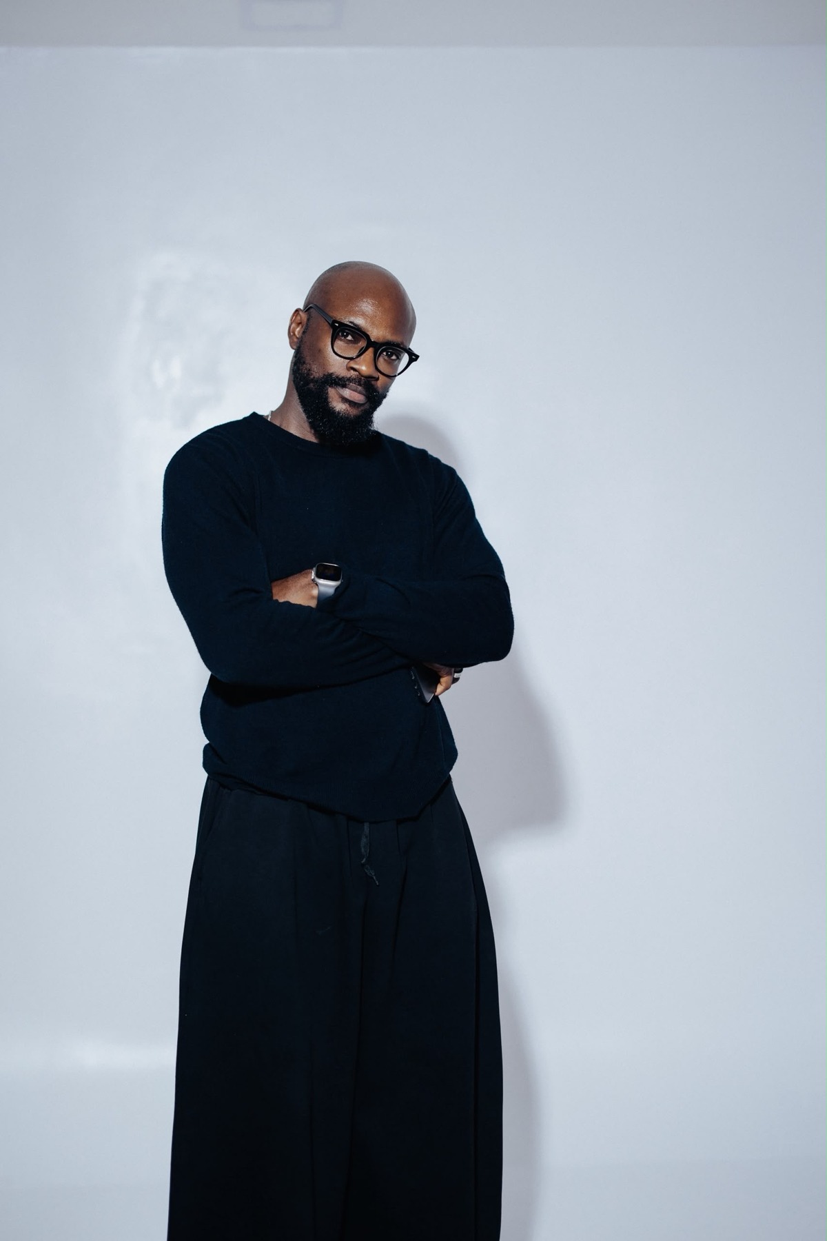 Bayo Farayola wearing black with glasses and arms folded