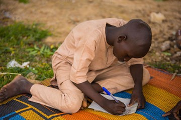 Child writing outdoors during a British Council documentary session