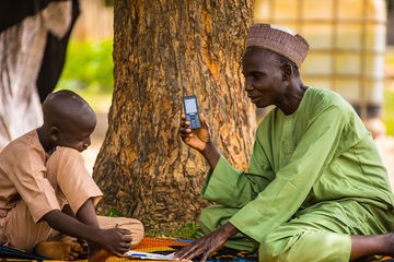 An adult and children sharing a learning moment beneath a tree