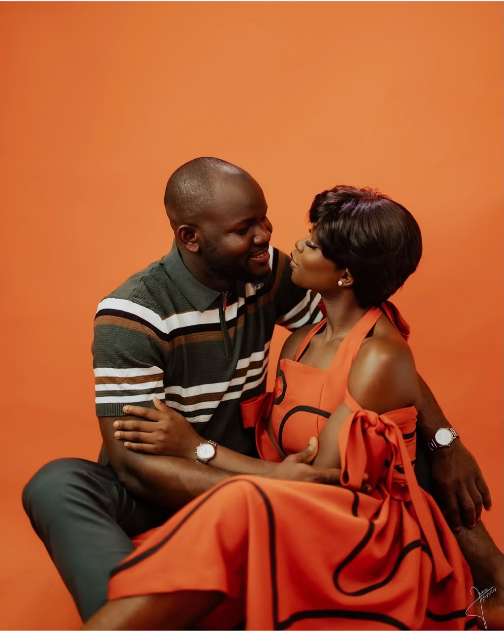 Seated couple leaning toward one another against an orange backdrop
