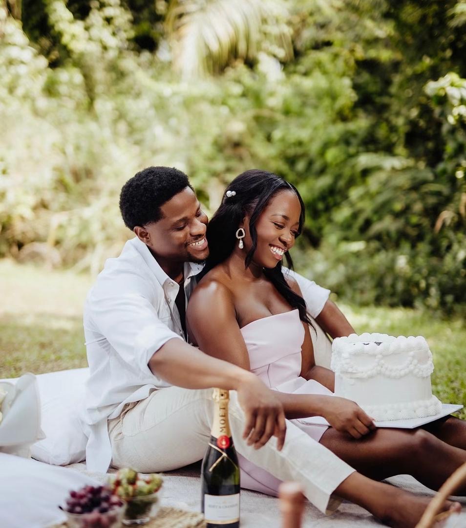 Couple smiling together while holding a cake at a garden picnic
