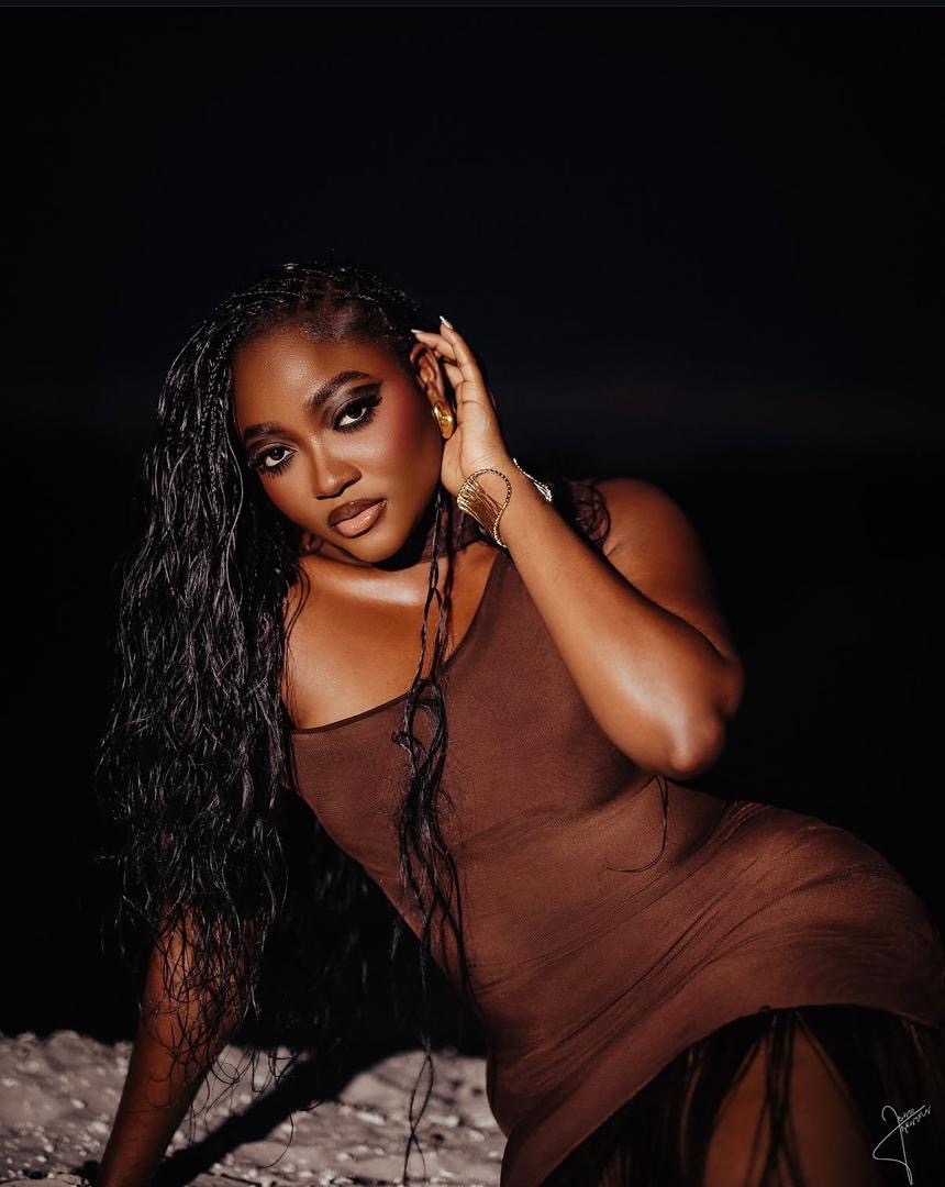 Woman with long braids wearing a brown dress against a dark background