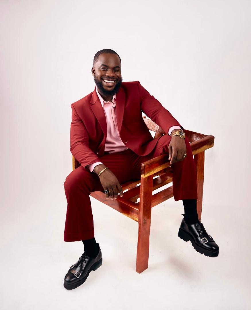 Smiling man seated in a burgundy suit against a white studio background