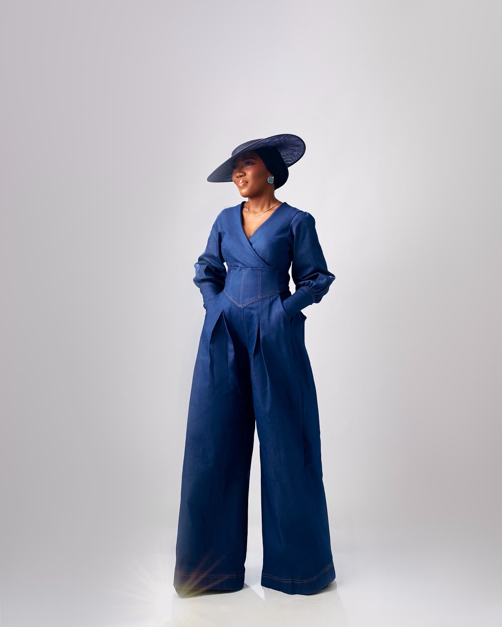 Studio portrait of a woman in a blue jumpsuit and wide brim hat