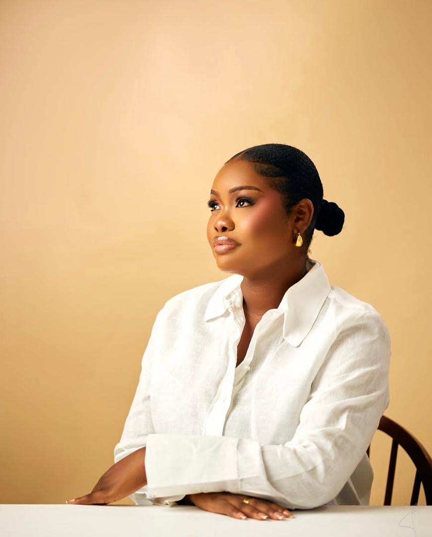 Woman in a white shirt seated at a table against a warm backdrop
