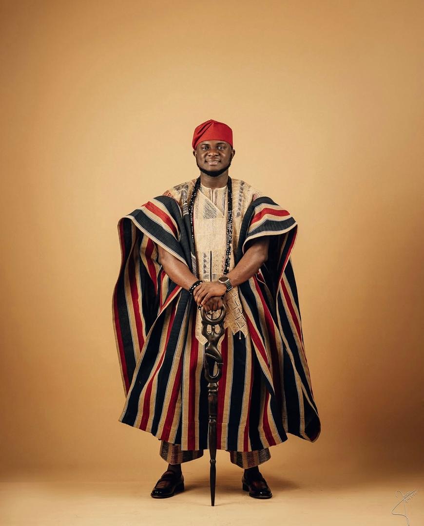 Man wearing striped traditional attire and a red cap, holding a staff