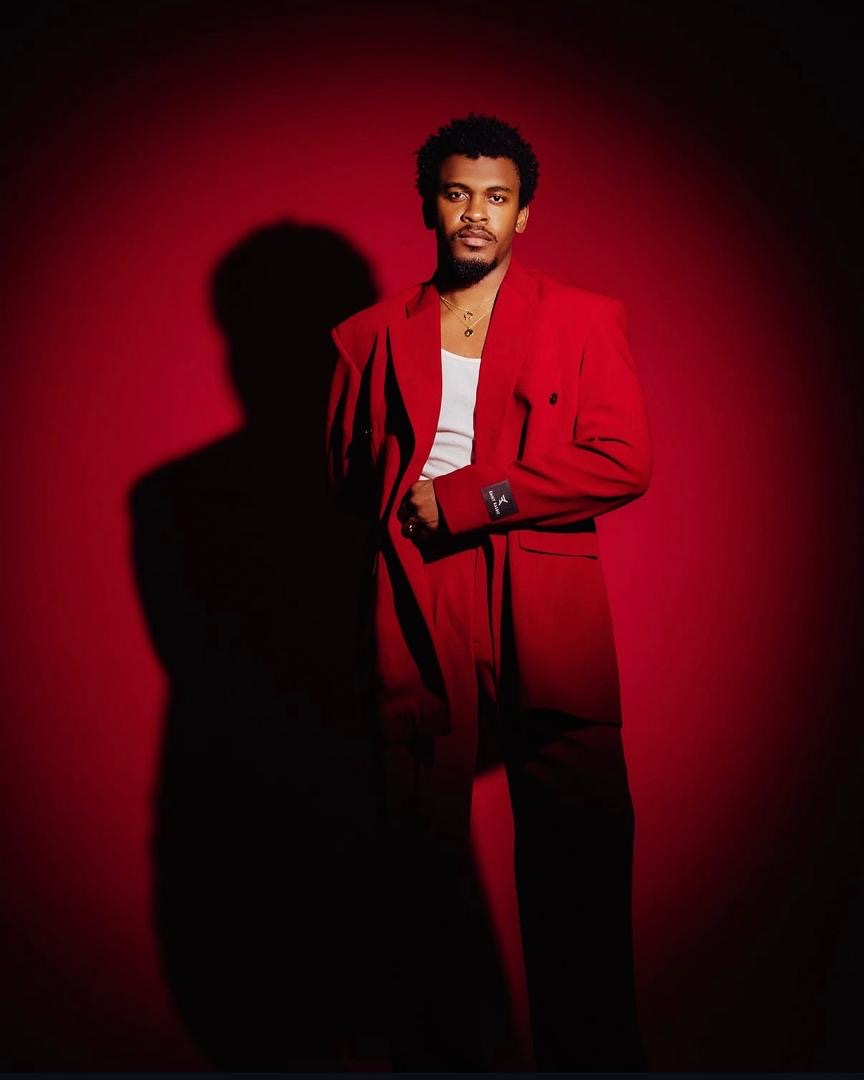 Studio portrait of a man in a red suit against a red background with a dramatic shadow