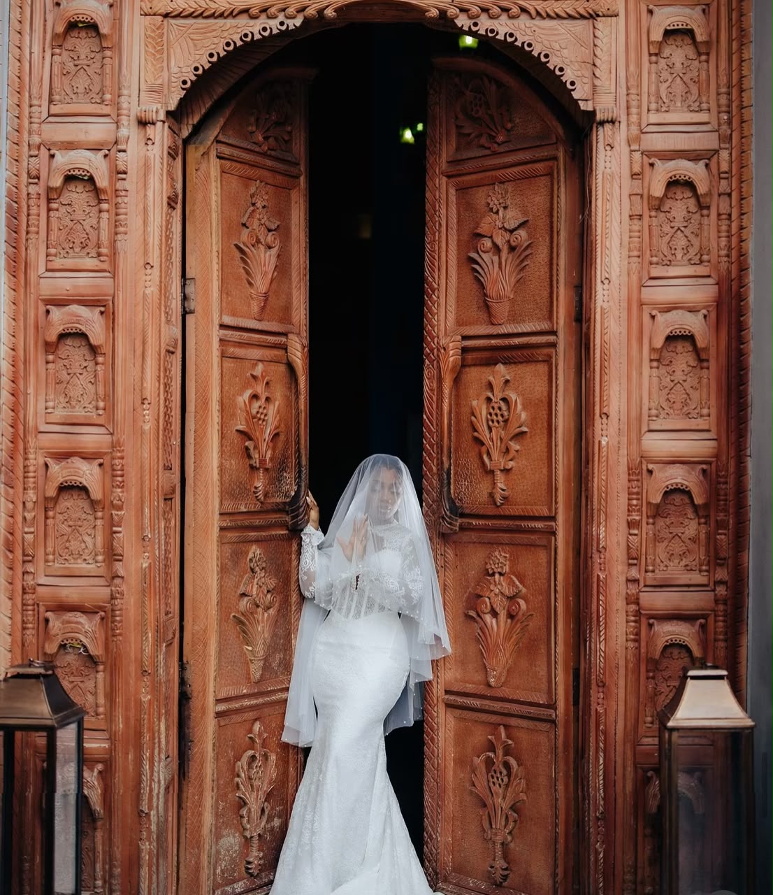 Bride under a veil standing in an ornate carved wooden doorway