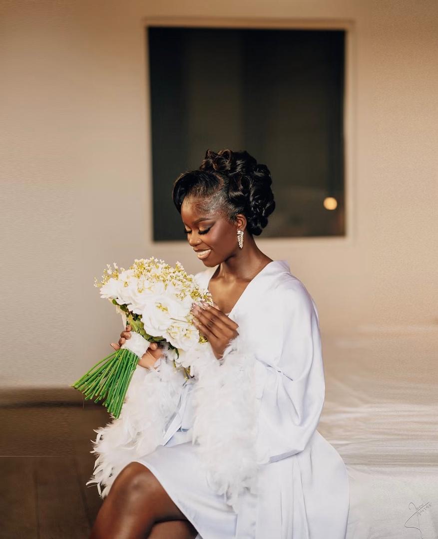 Bride in a white robe smiling down at her bouquet