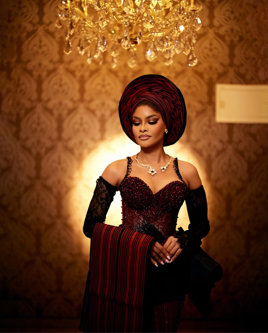 Bride in burgundy and black traditional attire beneath a chandelier