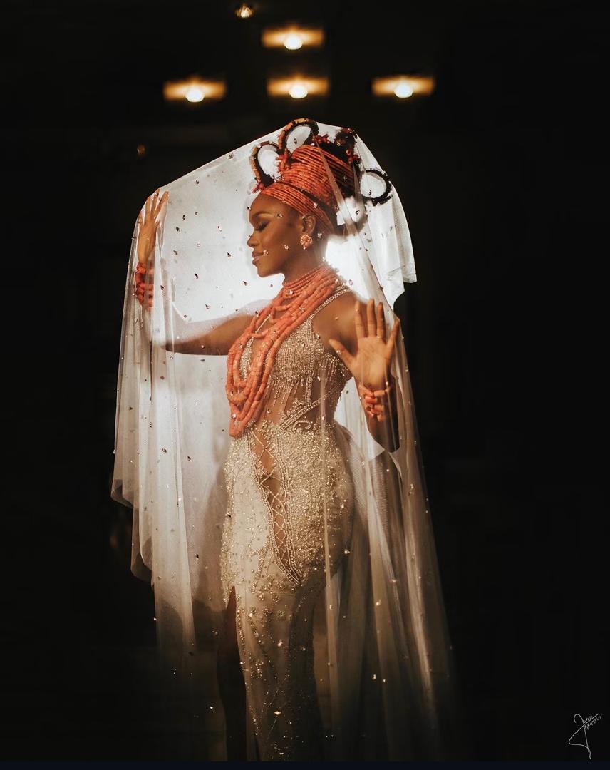 Bride in coral beads holding a sheer veil