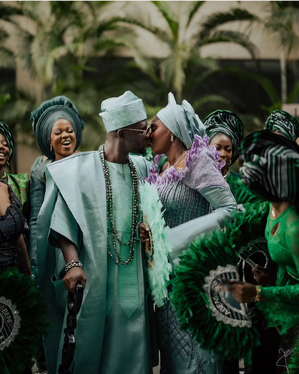 Newlyweds in mint traditional attire kissing among their wedding guests