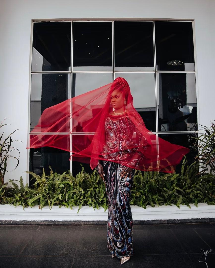 Bride with a flowing red veil before a large window