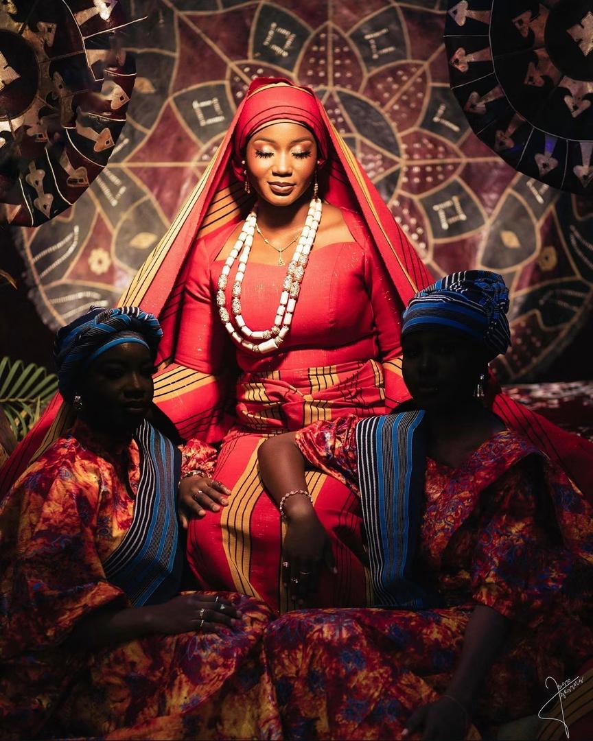 Bride in red traditional attire and white beads with two attendants in blue headwraps